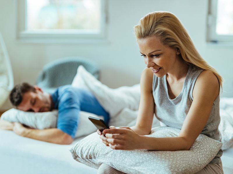 young happy woman holding phone while sitting on bed